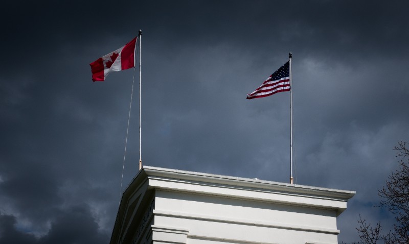 The US and Canadian flags flutter together on top of the Peace Arch border crossing between British Columbia and Washington State | US-Canada Border