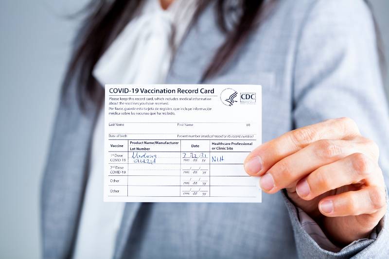 A caucasian businesswoman is showing her CDC issued COVID vaccination record card as a proof of immunization | ew York City vaccine rule