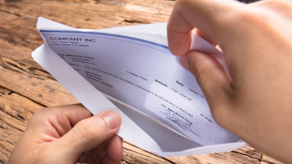 Cropped hands of businessman opening envelope with paycheck | 61% Of Americans Still Living Paycheck to Paycheck | featured