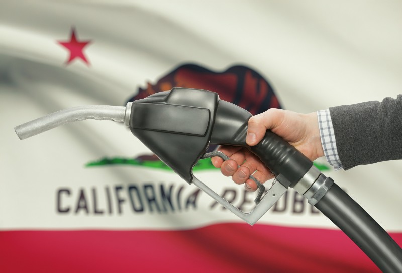 Fuel pump nozzle in hand with US states flags on background - California | California Gas Prices, Cruises, Overdoses & More