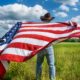 Man wearing cowboy hat waving American flag standing in grass farm-Democratic Party-SS-Featured