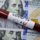 Closeup of positive covid-19 blood sample tube on top of one hundred dollars banknotes | COVID-Positive Americans Can Now Receive Free Antiviral Pills | featured