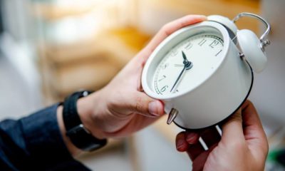 Male hand adjusting or changing the time on white clock | Senate OKs Bill to Make Daylight Saving Time Permanent | featured