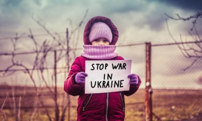 Little refugee girl with a sad look and a poster that says stop war in Ukraine | Putin is Committing Genocide in Ukraine, According to Biden | featured