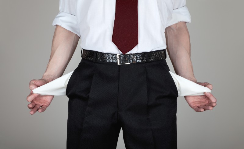 The businessman in a white shirt and black trousers shows his empty pockets | 2 out of 3 Americans Living Paycheck to Paycheck