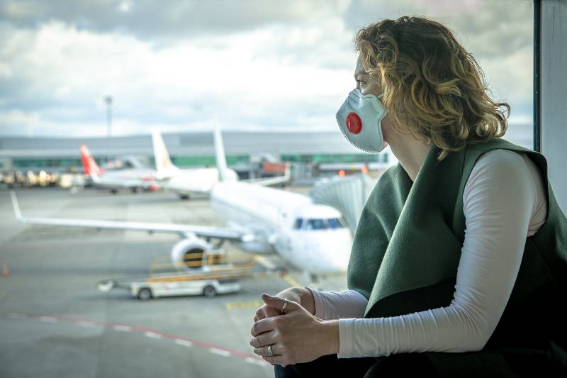 Woman with a mask on her mouth protects against the virus. She looks sad through the window at the airport on planes | Masks Optional For Several US Airlines