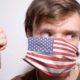 Young American man wearing USA face mask during coronavirus pandemic | Airlines Make Masks Optional After Judge Strikes Down Mandate | featured