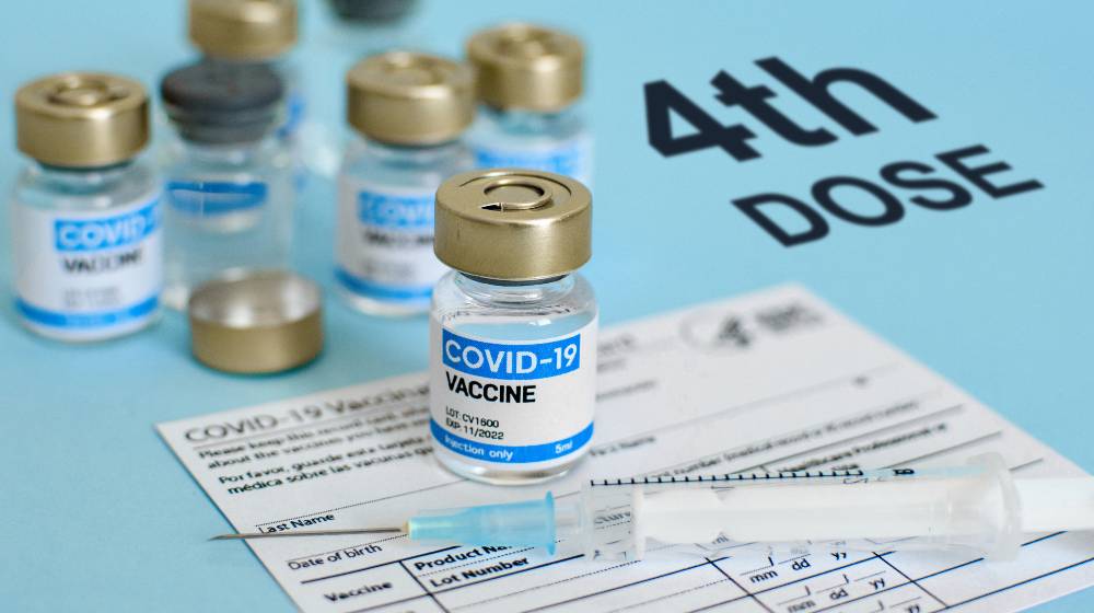 vaccine vial and syringe on CDC covid-19 vaccination record card Fourth | Is A 4th COVID Vaccine Dose Needed? Experts Remain Doubtful | featured