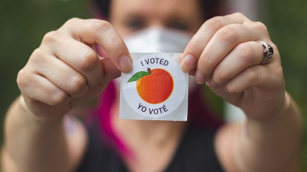 A Georgia Voter Wearing a Mask Holds Up her "I Voted" Sticker | Georgia Secretary of State: “Right Now, Georgia Remains Too Close to Call. There Will Be a Recount” | Featured