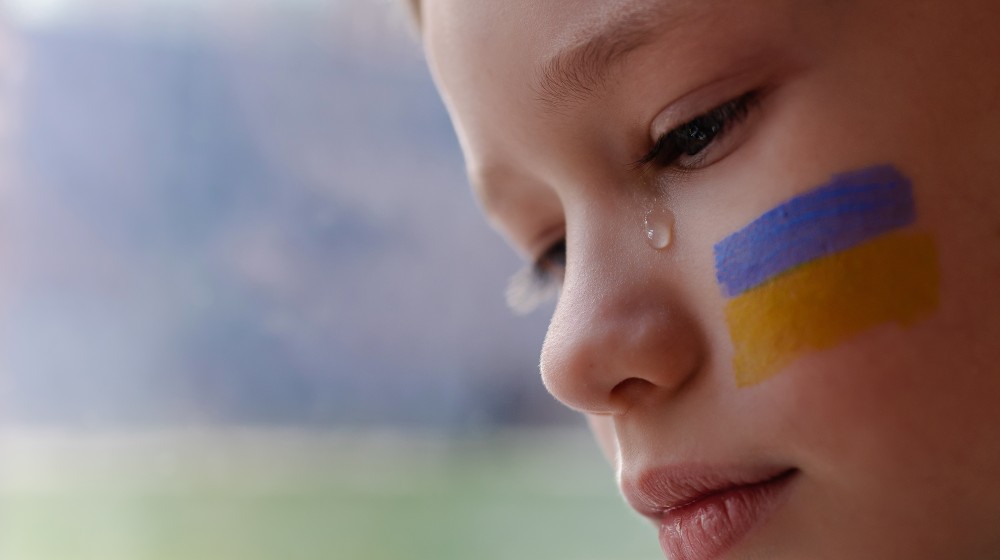A child with the flag of Ukraine is crying | US To Accept 10,000 Ukrainian Refugees | featured