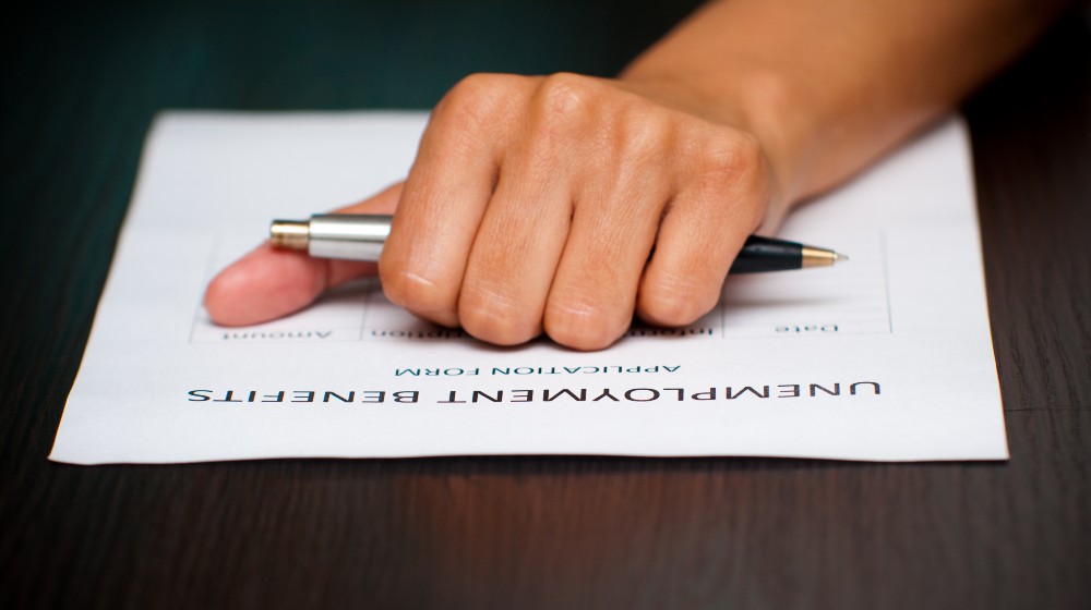 A female hand holding a pen over the unemployment benefits form to fill | Biden Won’t Ask Extension For Extra Jobless Benefits | featured