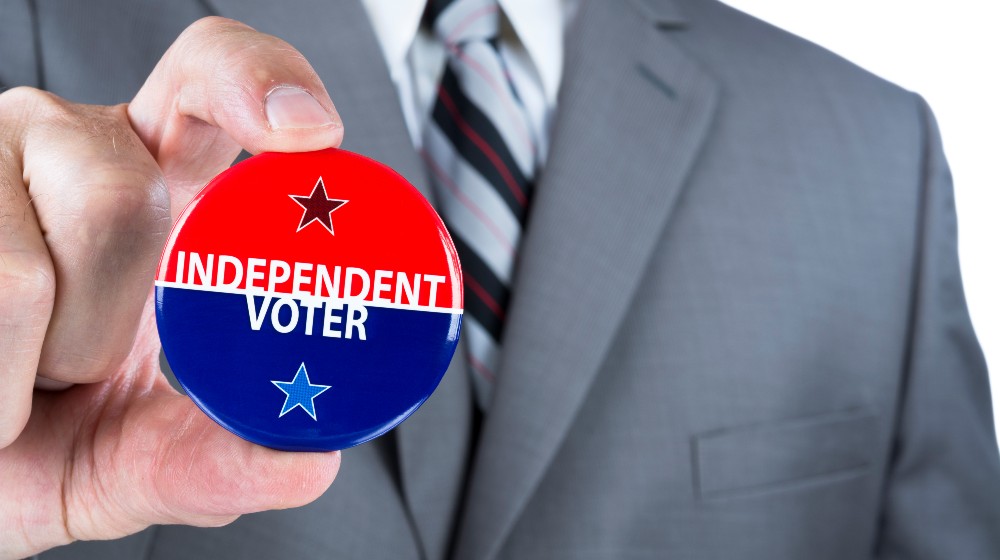 A man in a business suit holds out a political independent voter pin during elections | Independent Voters Are Dumping Joe Biden In Large Numbers | featured