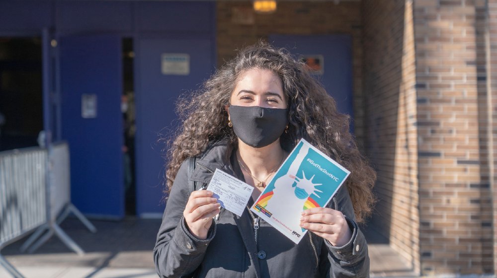 A woman displays her vaccination card and the “IGotTheShotNYC” banner after exiting the NYC Health Department Vaccine Hub-Vaccines By May-ss-featured
