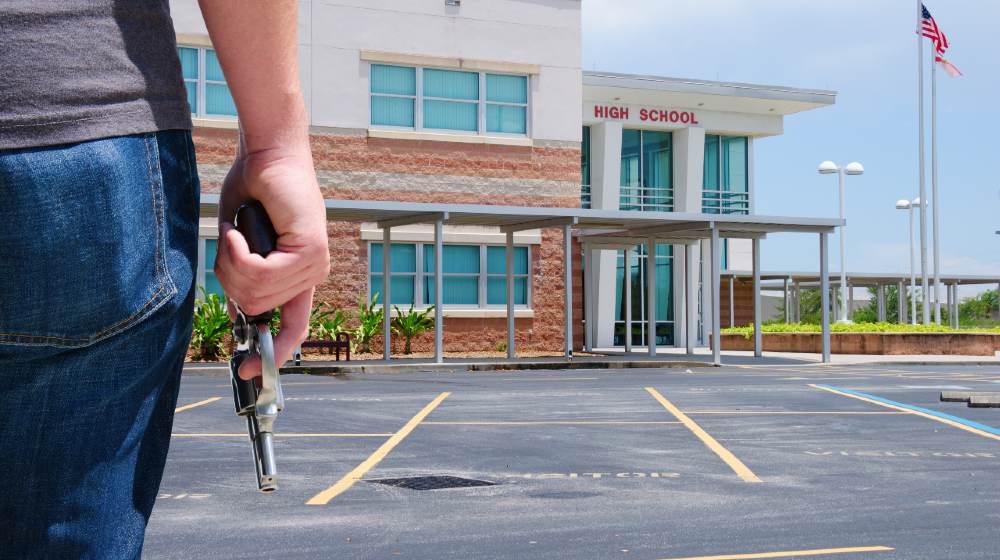 A young man with a pistol gun is standing in front of a high school preparing to commit a crime-School Shooter | School Shooter Dead, Officer Wounded in Knoxville Incident | Featured