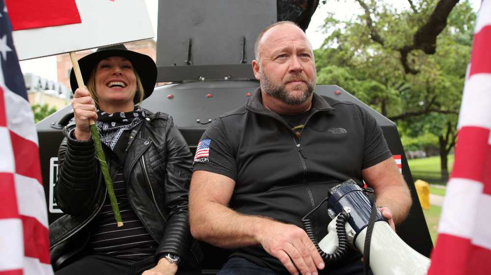 Alex Jones, with his wife Erika Wulff Jones, sits in the bed of an armored truck | InfoWars Files for Bankruptcy As Alex Jones Faces Legal Costs | featured