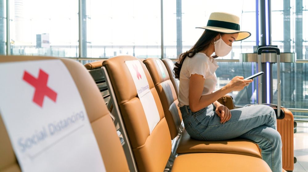 Female Tourist wearing Mask using Mobile Phone | Travelers Must Assess Risk When Flying to Avoid COVID-19 | Featured