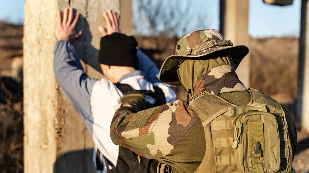 Back view of man in uniform unknown military soldier or special forces police arresting and searching criminal illegal migrant or terrorist in sunny day | Homeland Security Issues New Rules When Arresting Migrants | featured