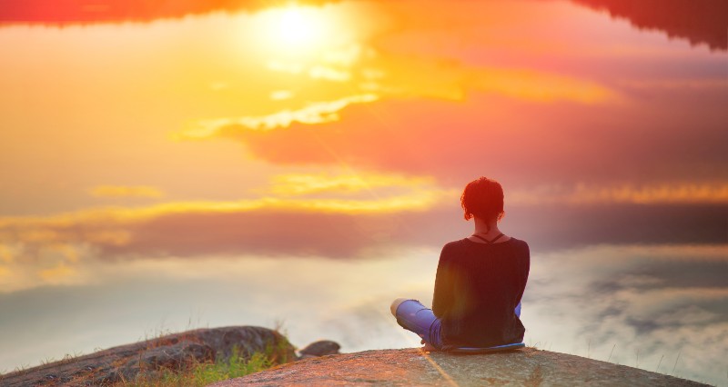 Beautiful woman sits in a pose of a lotus on high place with amazing view of the lake sunset | Balance of the Universe