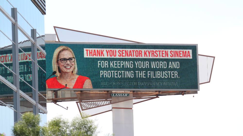 Bought by Election Transparency Initiative, a highway billboard sign thanks Senator Kyrsten Sinema for protecting the filibuster | Democrats’ Election Bills Good As Dead As Manchin and Sinema Help Republicans Keep The Filibuster | featured
