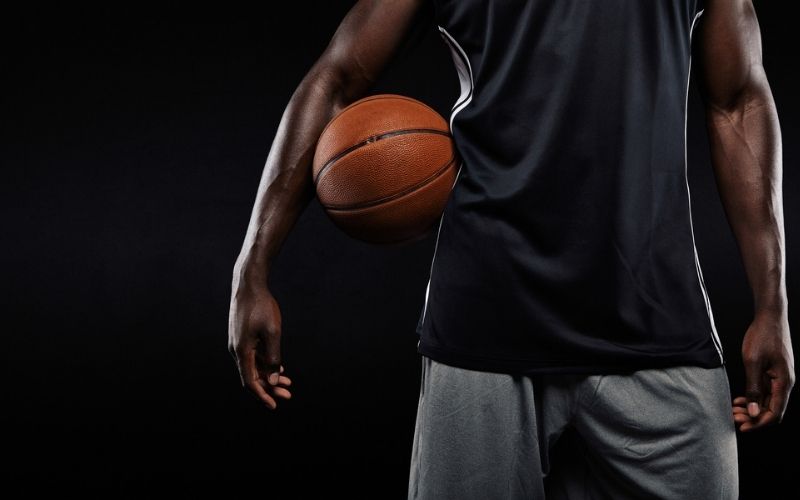 Cropped Image of Afro American Basketball Player Holding a Ball Against Dark Background | Jonathan Isaac Stands During National Anthem and Doesn’t Wear BLM Shirt; Jersey Sales Surge | Featured