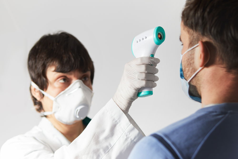 Doctor screening the temperature of a man using an infrared forehead thermometer-Temperature and Symptom Screenings Are Inadequate in Detecting COVID-19 Cases-ss-Featured