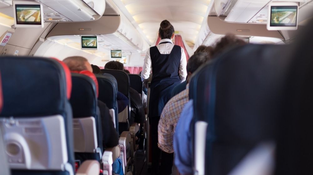 Flight attendant walking down the aisle of a passenger plane-Flight Attendants Union Wants Trump Supporters To Be Banned From Flights-ss-featured