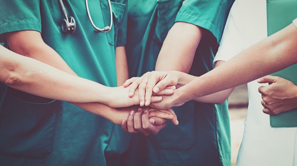Doctors nurse coordinate hand | 53-Year-Old Health Care Worker from Michigan Dies Alone from Coronavirus | Featured