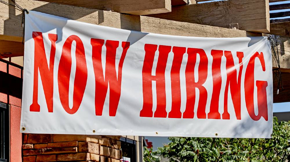 Large now hiring sign posted in the front of a business | Kentucky Governor Offers Citizens $1,500 To Return To Work | featured