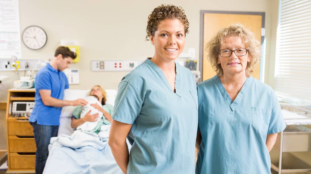 Portrait of confident nurses standing against couple with newborn baby at hospital