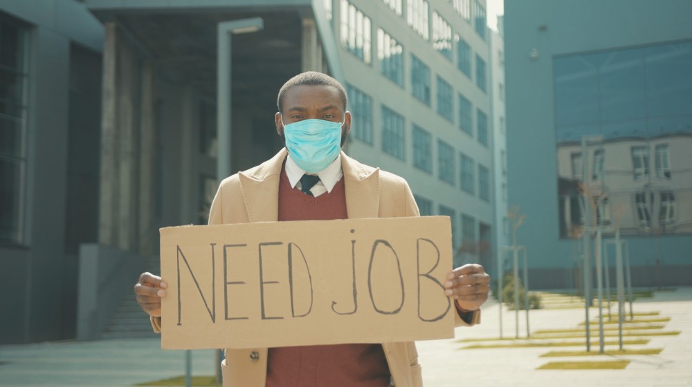 Portrait young african american man wear masks holding poster cardboard with Crisis | Latest Jobless Rate Totals 214,000, Lower Than Expected | featured