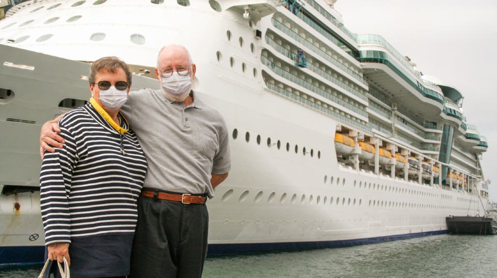 Senior Couple Wearing Face Masks Standing In Front of Passenger Cruise Ship-Cruise Lines Stocks-ss-featured