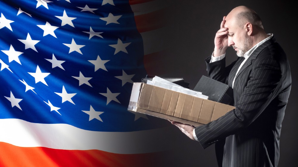 The dismissed employee clutched his head against the background of the US flag-Real Unemployment-ss-featured