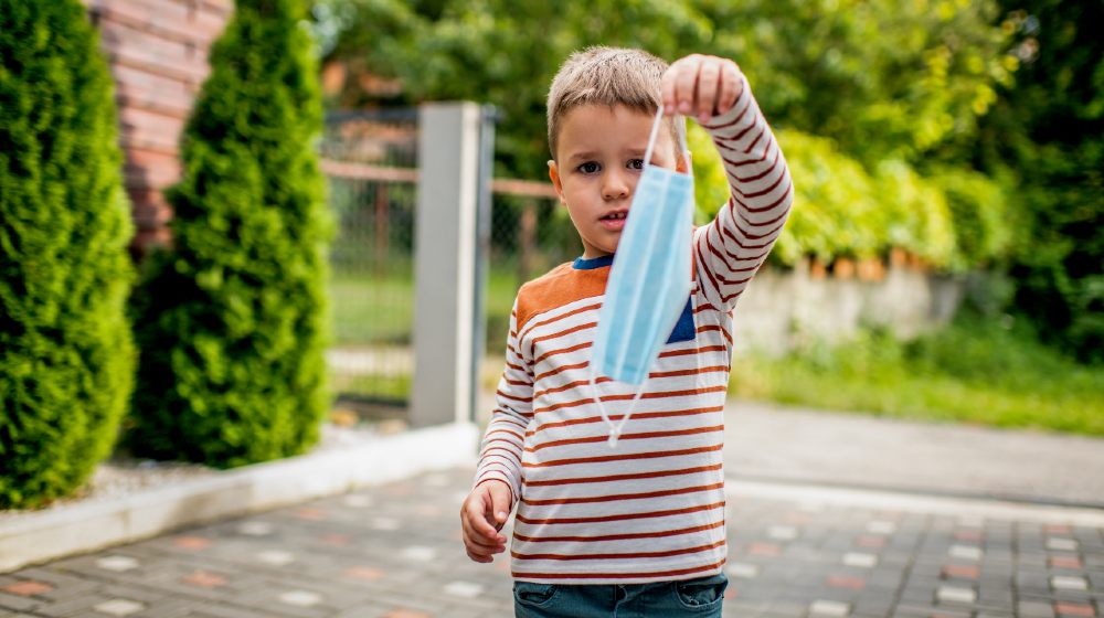 The upset boy holds out the mask, refuses to take on it on the Playground. The concept of not wearing, refuses to put on masks-Mask Mandate-ss-featured