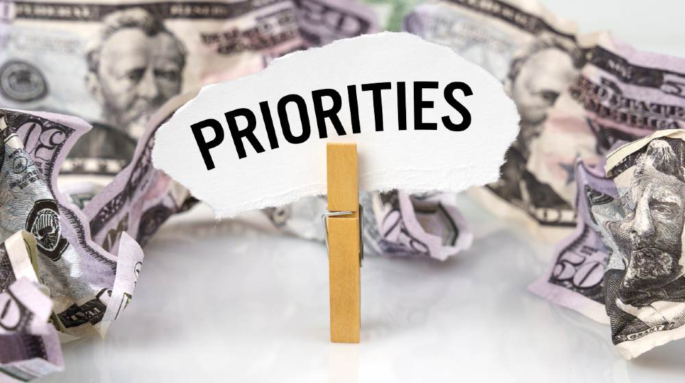 There are dollars on the table and there is a clothespin with paper on which it is written - PRIORITIES | 5 Most Urgent American Priorities | featured