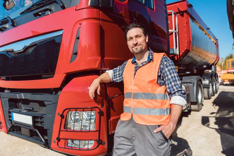 Truck driver in front of his freight forward lorry looking at camera | US Suffering From Shortage of Truck Drivers
