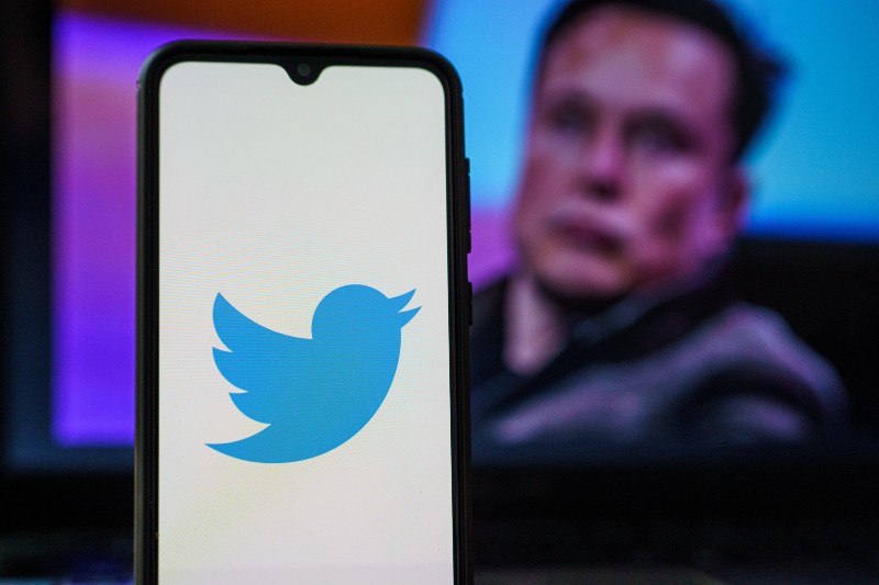Twitter logo on smartphone and Elon Musk in the background | Musk Buys Twitter At Nearly 40% Premium 