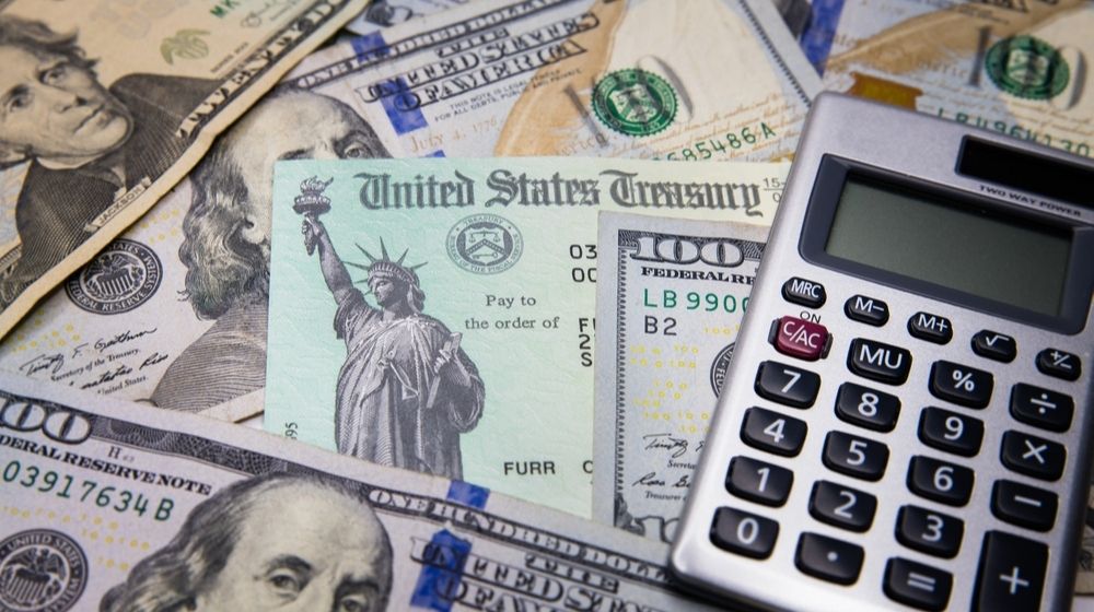 United States Treasury Check Surrounded by Calculator and US Currency $100 bills Illustrating IRS | Congress Set for Another Round of Coronavirus Relief Negotiations | Featured