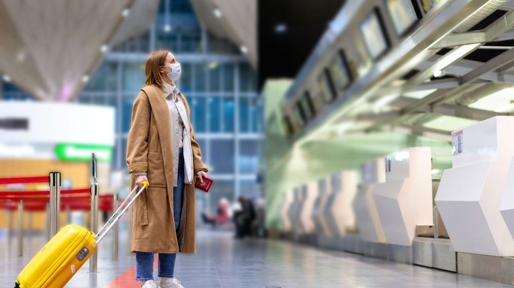 Woman with Luggage Stands at Almost Empty Check-in Counters | U.S. Officials Looking to Shorten Quarantine Time for New York-London Travels