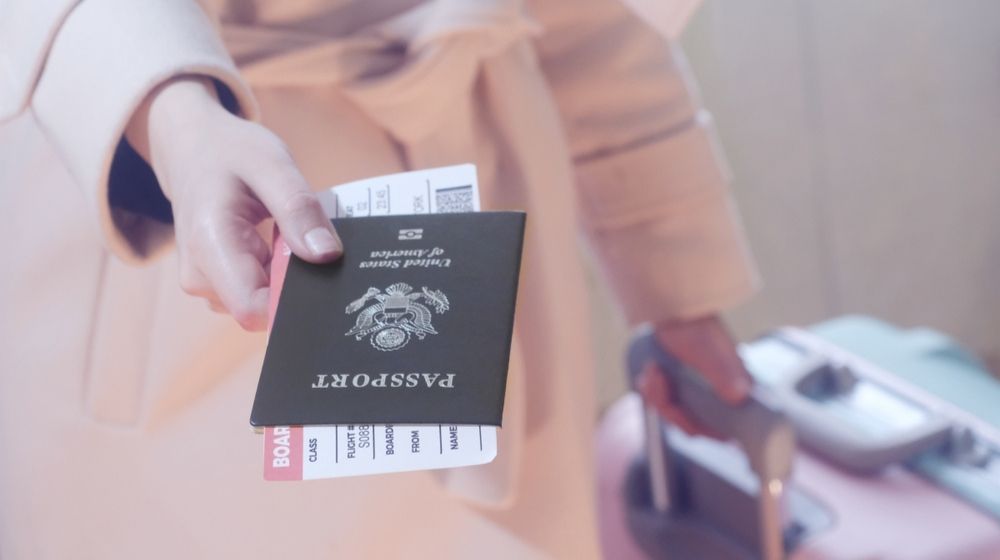 Woman with suitcase holding passport and boarding pass-2021 Travel Could Include Vaccine Passports-ss-featured