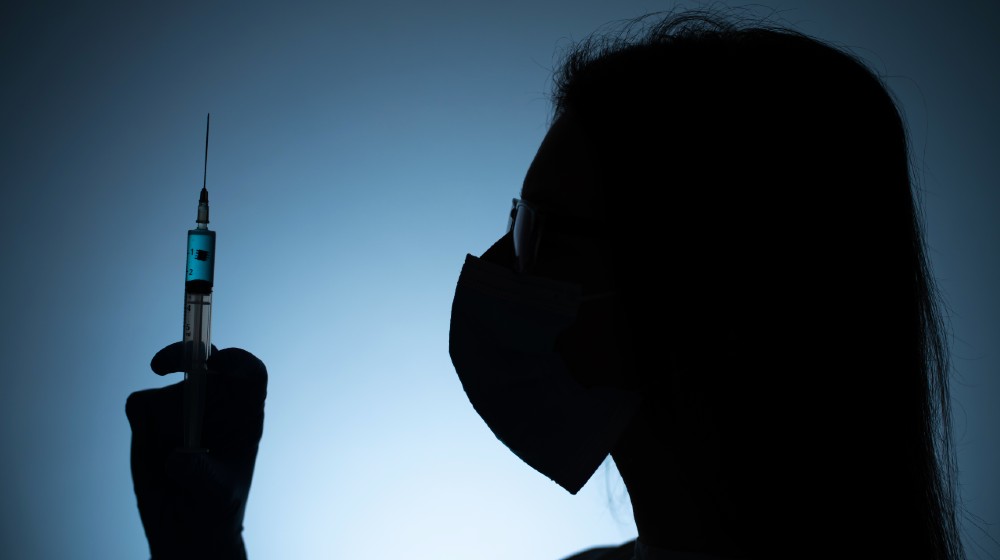 Young female doctor in a medical mask and gloves holds a syringe with a coronavirus vaccine | Fact - Checking Vaccination Conspiracy Theories | featured