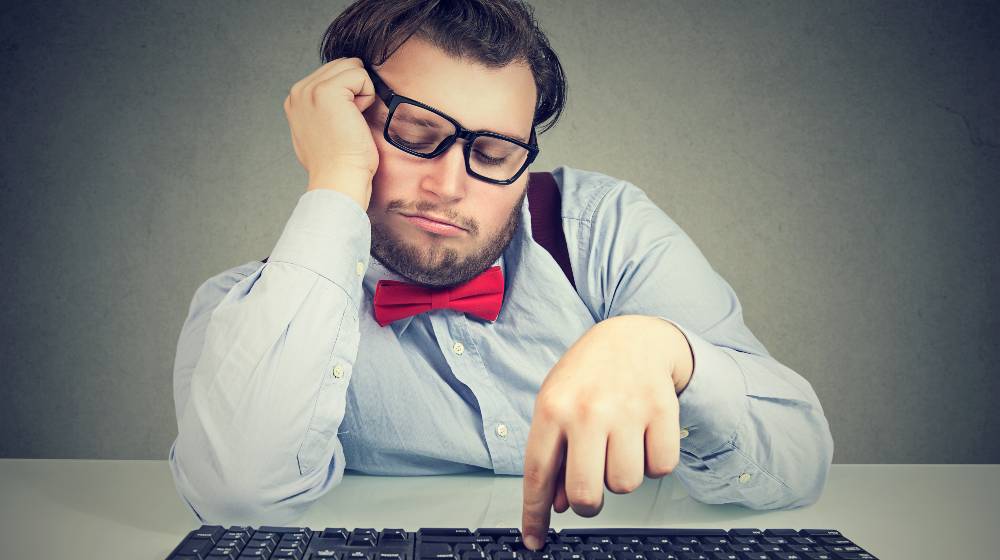 Young obese man sitting at workplace and procrastinating being lazy and distracted | Some Ways To Avoid Procrastination | featured
