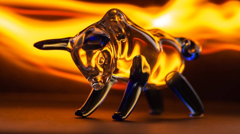 bull figurine on a black background in the glare of fire | How a Gold Bull Run Is Setting Up Beautifully | Featured