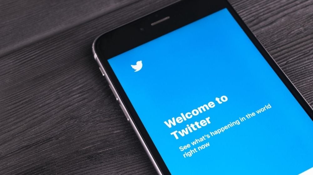 iPhone 7 Plus on Wooden Table with Open Twitter App | Twitter Apologizes for Accidentally Labeling Some Tweets as Misleading | Featured