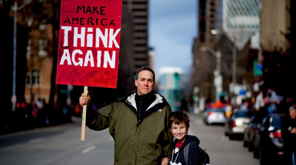 man and his son holding a protest banner Make America Think Again | Divisions on Impeachment Reflect Deep American Political Divide
