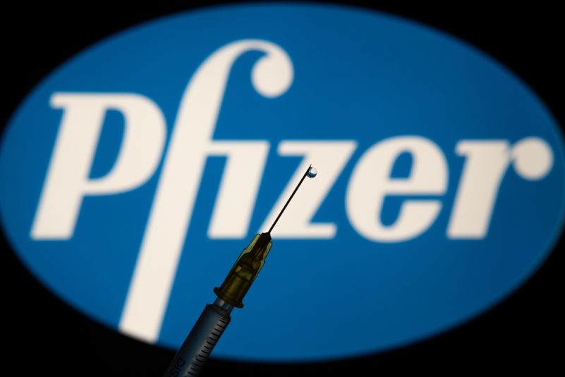 medical syringe in front of Pfizer Logo | From CNN, Here Are the CNN 5 Things You Need to Know